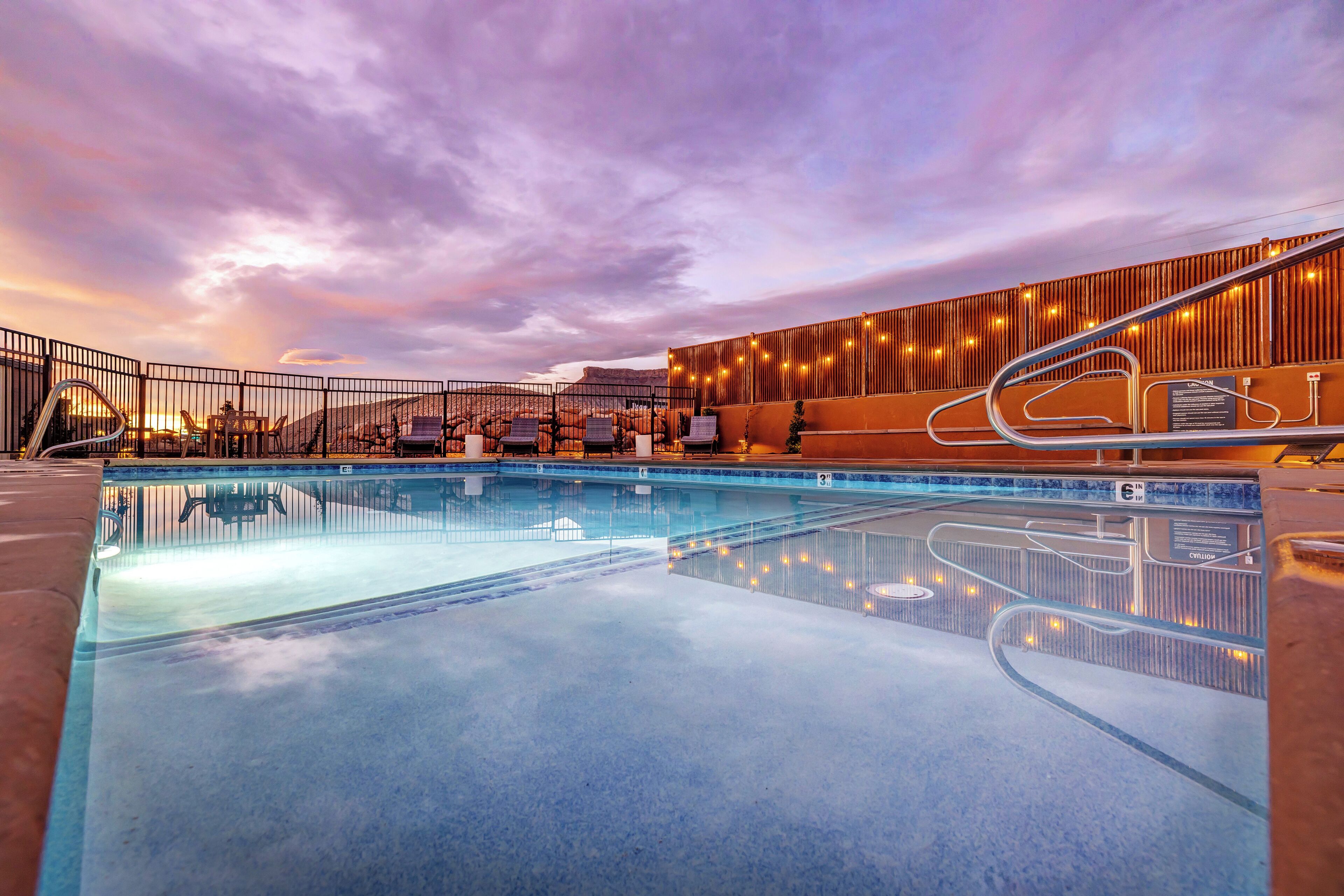 Piscina con vistas a un paisaje montañoso, zona de estar cubierta y barandilla.
