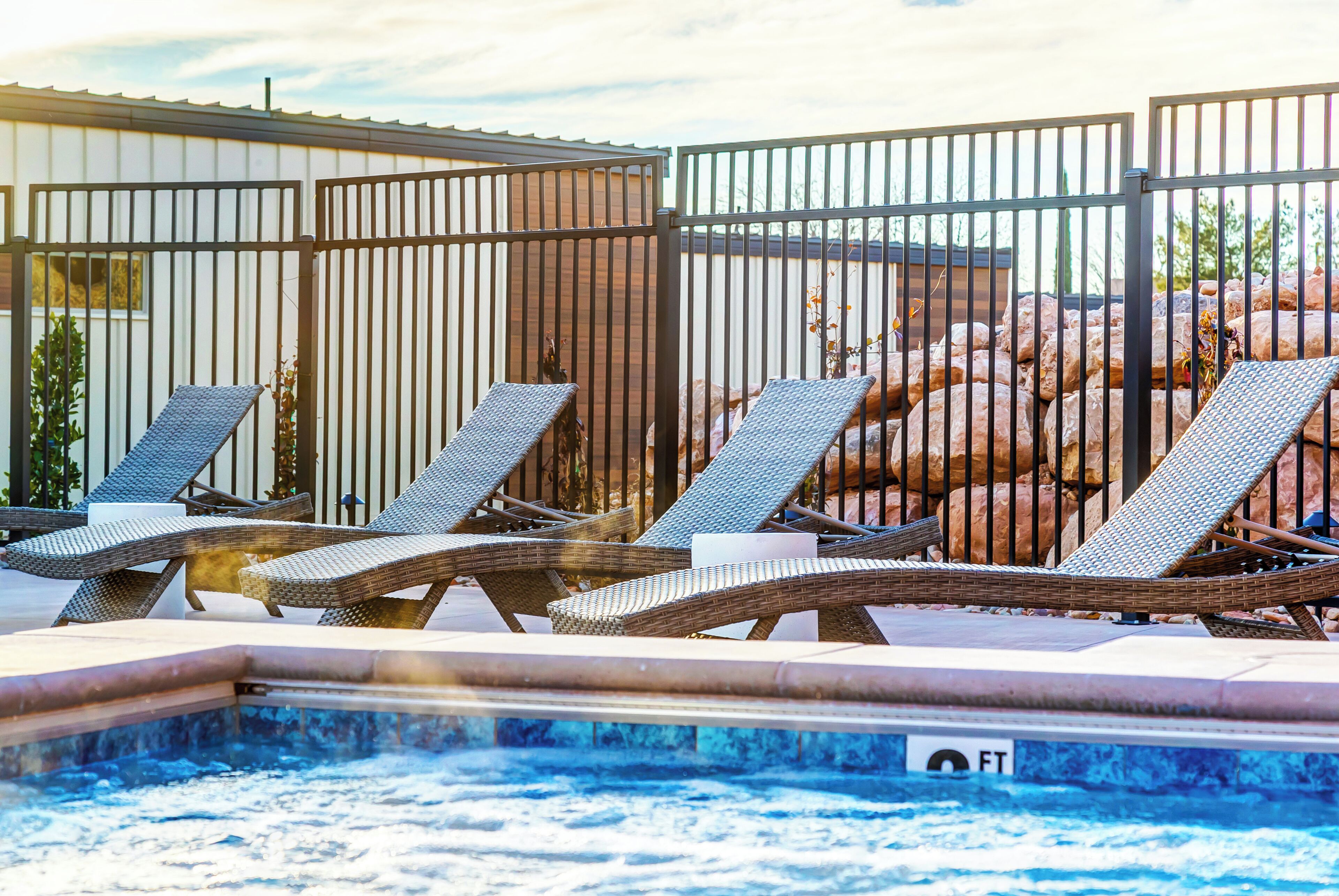 Un área de piscina con sillones de descanso y un jacuzzi, rodeada por una valla metálica.