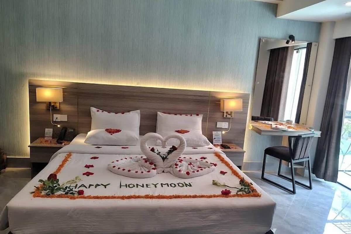Une chambre d’hôtel avec un lit décoré d’un arrangement floral en forme de cœur et sur lequel est brodé le message « JOYEUX LUNE DE MIEL ».