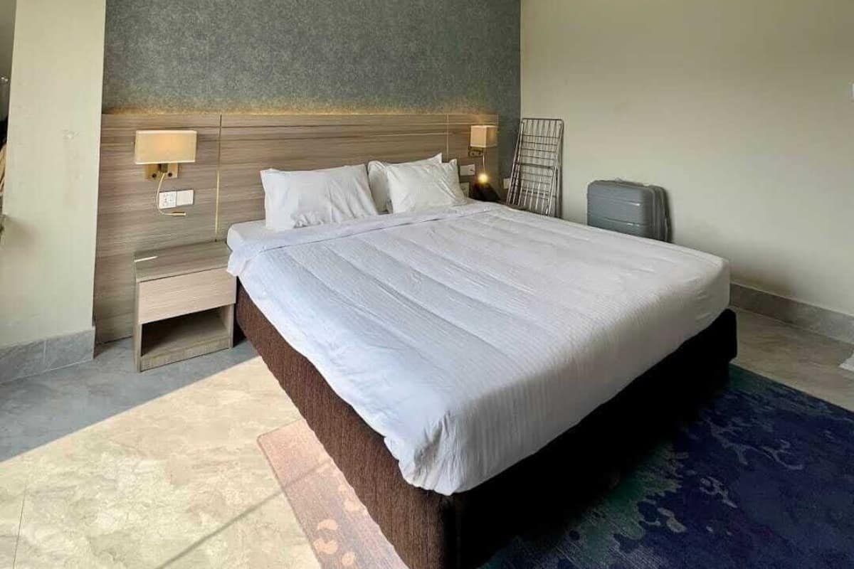 Une chambre d’hôtel moderne avec un grand lit, une table de chevet, une lampe et un petit coin salon.