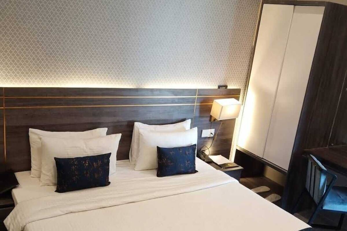 Une chambre d’hôtel avec un grand lit, deux oreillers, une table de chevet avec une lampe et une armoire.