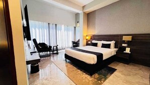 Une chambre d’hôtel moderne dotée d’un grand lit, d’un bureau avec une chaise, d’une télévision et d’une grande fenêtre avec des rideaux.