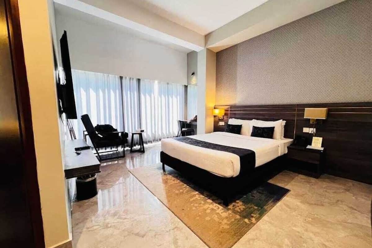Une chambre d’hôtel moderne dotée d’un grand lit, d’un bureau avec une chaise, d’une télévision et d’une grande fenêtre avec des rideaux.