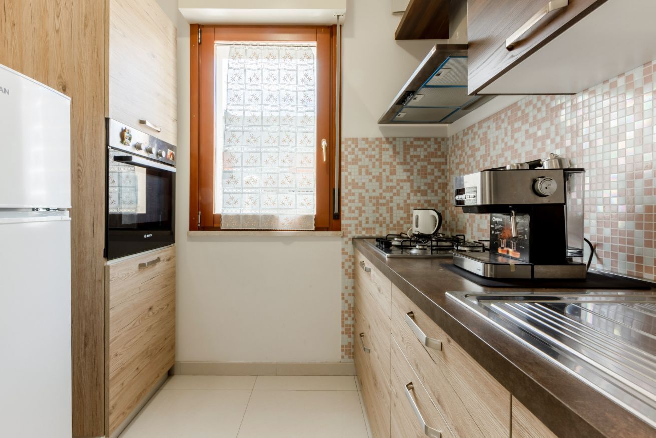 Una cocina compacta con horno integrado, cafetera y ventana con cortina estampada.
