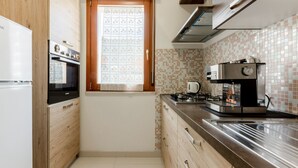 Una cucina compatta con forno integrato, macchina del caffè e finestra con tenda decorata.
