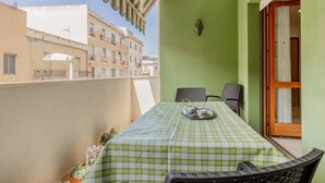 Un balcone con una tovaglia a scacchi, due sedie, un vassoio con tazzine da tè e vista sugli edifici circostanti.
