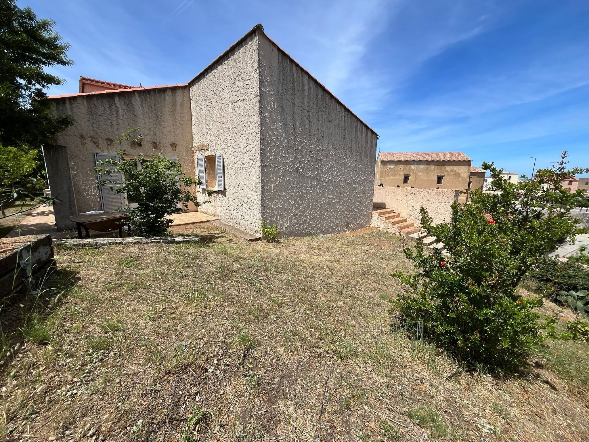 Un edificio in pietra con un piccolo giardino, un carriola e una scala che conduce a un altro edificio.