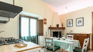 Uma cozinha com fogão a gás, uma mesa de jantar com cadeiras, lareira e janela com cortinas.