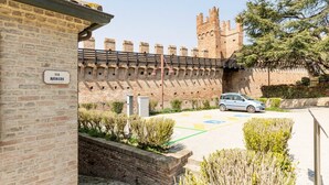 Paredes de tijolo com uma placa indicando 'Via Rubini', área pavimentada com um carro e uma estrutura semelhante a um castelo ao fundo.