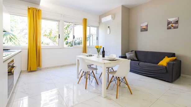 A modern living room with a dining table, sofa, and large windows with curtains. - GuestHost - Charming 64 sqm apartment, ideal for three people, located on the mezzanine floor of a building without a lift.The property is located in a privileged position, close to Piazza della Rinascita, the hub of city life in Pescara, and a stone's t (Pescara)