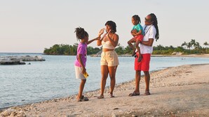 A family of four by a beach with a calm sea and a clear sky. - 3-bedroom Gated Beachfront Villa with Pool- Luxury & Security. Pet-Friendly! (Saint Ann's Bay)