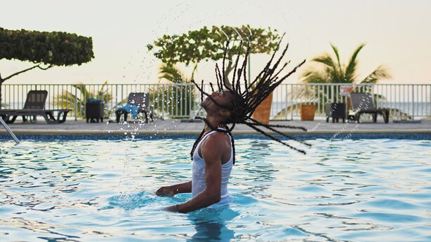 A person in a swimming pool with a view of lounge chairs and a palm tree in the background. - 3-bedroom Gated Beachfront Villa with Pool- Luxury & Security. Pet-Friendly! (Saint Ann's Bay)