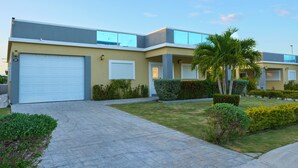 A modern two-story building with a garage, well-maintained lawn, and palm trees. - 3-bedroom Gated Beachfront Villa with Pool- Luxury & Security. Pet-Friendly! (Saint Ann's Bay)