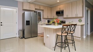 A modern kitchen with light wood cabinets, stainless steel appliances, and a central island with bar stools. - 3-bedroom Gated Beachfront Villa with Pool- Luxury & Security. Pet-Friendly! (Saint Ann's Bay)