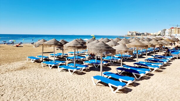 A beach with rows of blue lounge chairs and thatched umbrellas. - Cozy Bungalow with Private Terrace and Communal Pool in Torrevieja (Torrevieja)