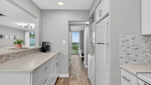 A modern kitchen with white cabinets, a coffee maker, and a view to a balcony. - Ocean Breeze Condo | Ocean Views | Steps To Beach | Pool | Flagler/Ormond Beach (Ormond Beach)