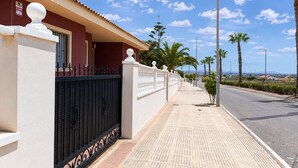 Una propiedad costera con un camino pavimentado, un portón de metal negro y palmeras.