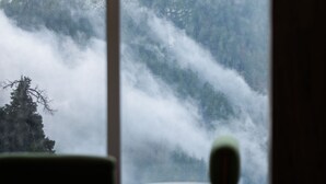 A room with a large window overlooking a mountainous landscape with dense forests and mist. - EAFR Hotel (Nathia Gali)