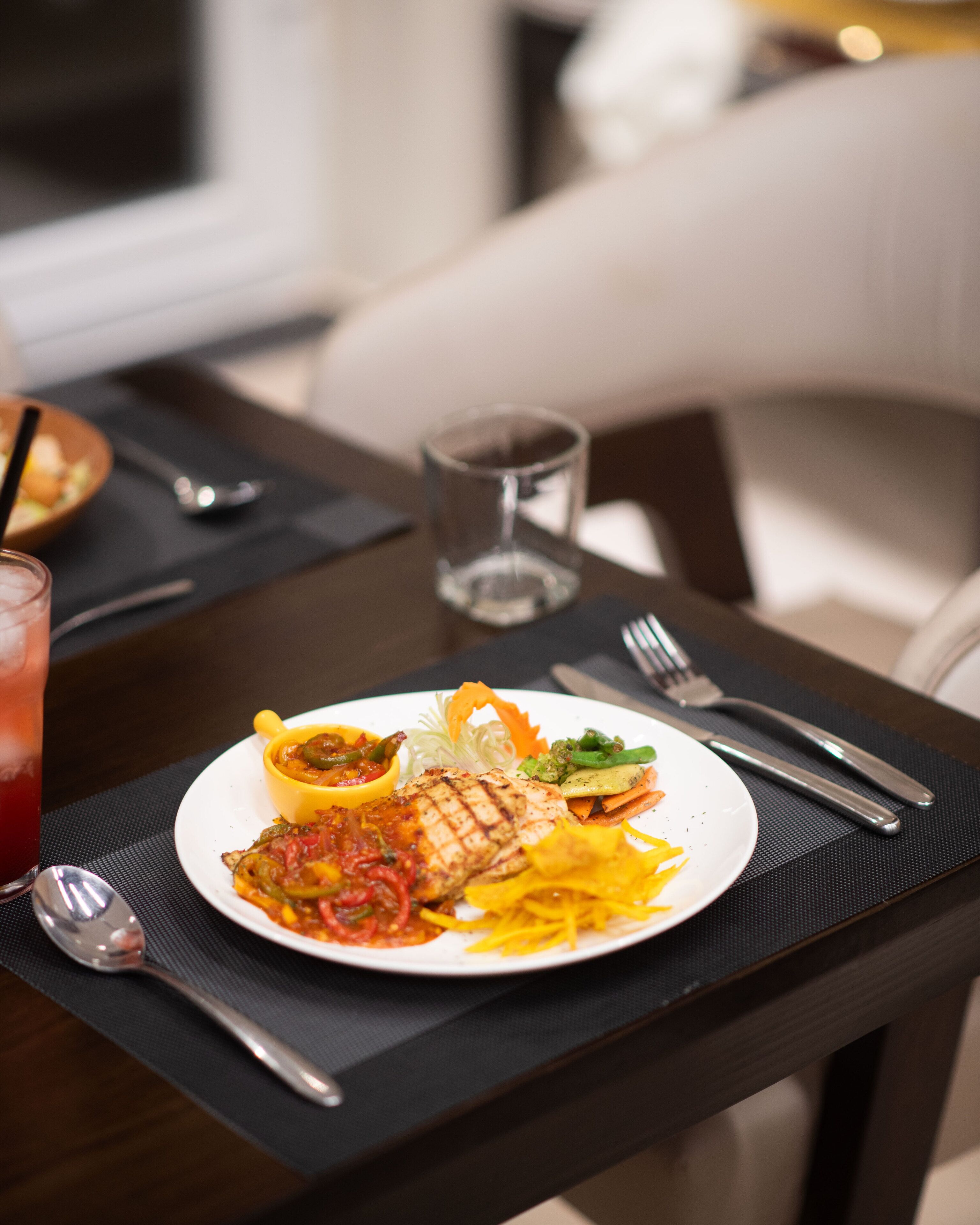 A dining table with a plate of food, a glass of red drink, and cutlery.