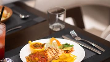 A dining table with a plate of food, a glass of red drink, and cutlery.