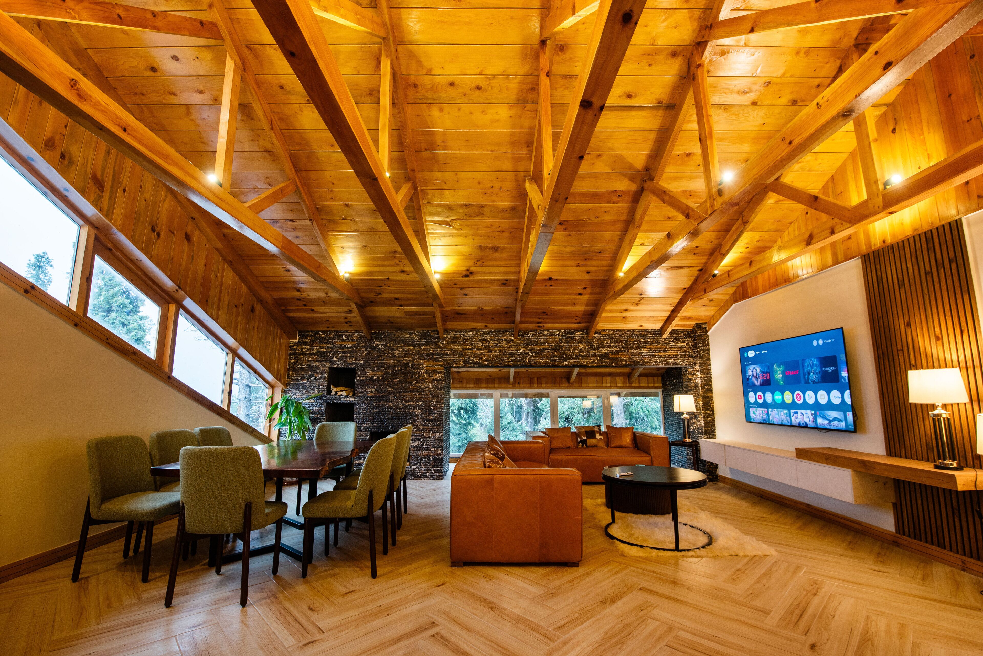 Un'ampia zona giorno con soffitto in legno, parete in pietra e un grande schermo televisivo.