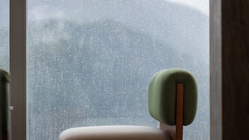 Una silla con reposacabezas verde y patas de madera, ubicada frente a una ventana con vistas a una cadena montañosa.