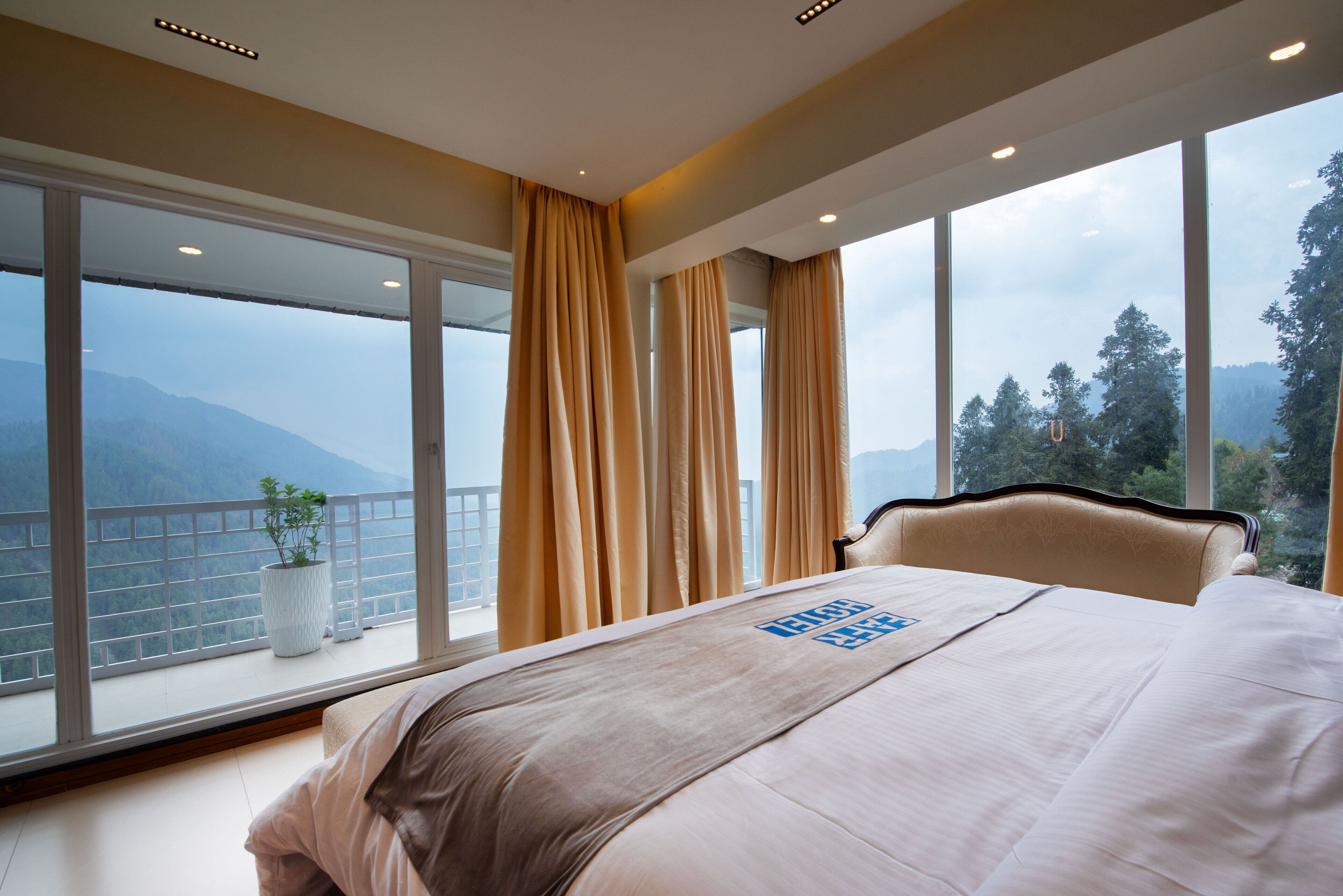 A hotel room with a large bed, a view of mountains, and a balcony with a potted plant.