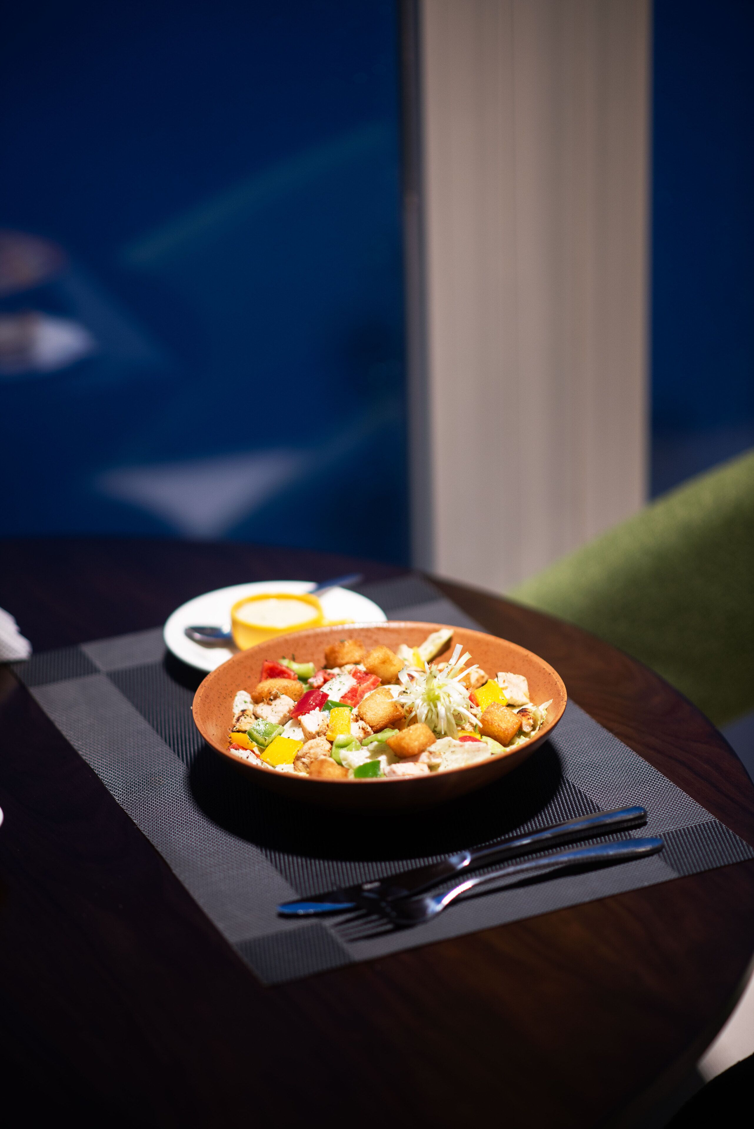 A dining table with a plate of food, a bowl of sauce, and chopsticks.