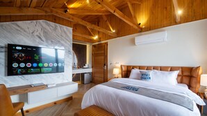 A modern hotel room with a large flat-screen TV mounted on a marble wall, a wooden ceiling, a bed with a headboard, and a bench. - EAFR Hotel (Nathia Gali)