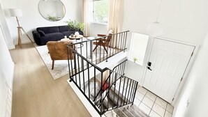 Un vaste espace de vie agrémenté d’un canapé aux couleurs sombres, d’un miroir rond et d’un ventilateur de plafond.
