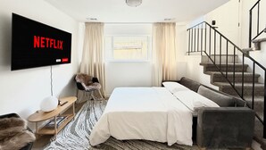Une chambre à coucher moderne avec un lit, un canapé, un téléviseur fixé au mur et un escalier.