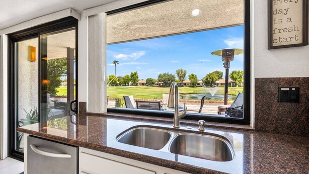 A kitchen with a granite countertop, stainless steel sink, and a view of a golf course through a large window. - Golf Course Views, Pool, Spa, Dine Al Fresco (Rancho Mirage)