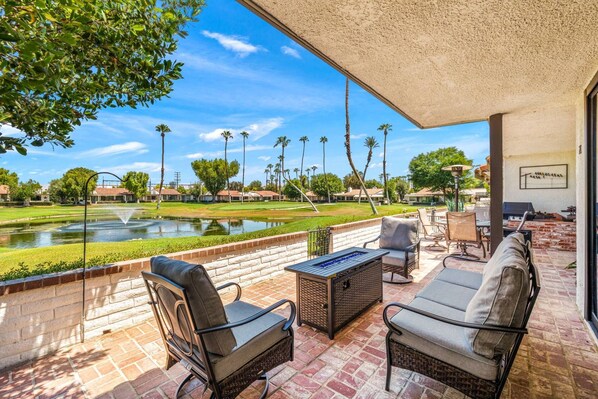 A covered patio with wicker furniture, a view of a golf course, and a pond.