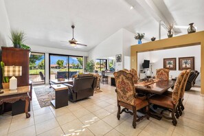 A spacious living room with a dining area, large windows, and a ceiling fan.