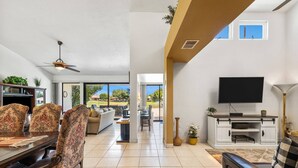 A spacious living area with a dining table, floral chairs, a sofa, a television, and a fireplace. - Golf Course Views, Pool, Spa, Dine Al Fresco (Rancho Mirage)