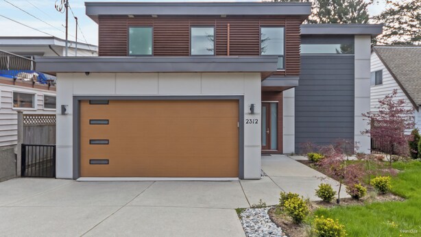 A modern two-story house with a garage, a visible address number, and a well-maintained front yard with small plants and a gravel pathway.