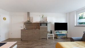 Un apartamento moderno con kitchenette, un televisor de pantalla plana, una cama con manta amarilla y un ventanal con vistas.