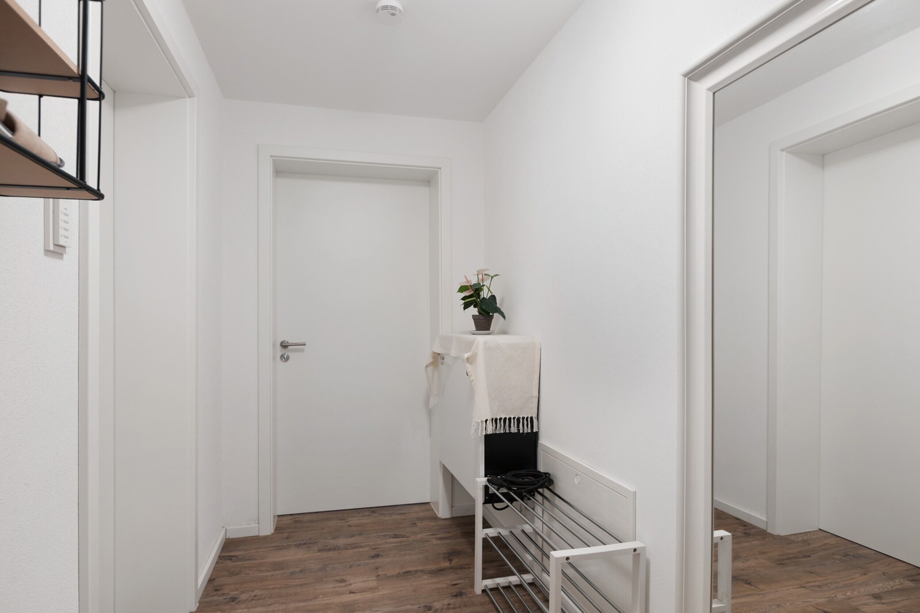 Un pasillo con una puerta blanca, una planta sobre una mesa y un tendedero.