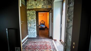 A hallway with a stone wall, a patterned rug, and a bed in the distance.