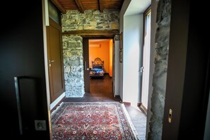 A hallway with a stone wall, a patterned rug, and a bed in the distance. - Piazzaga565 (Torno)