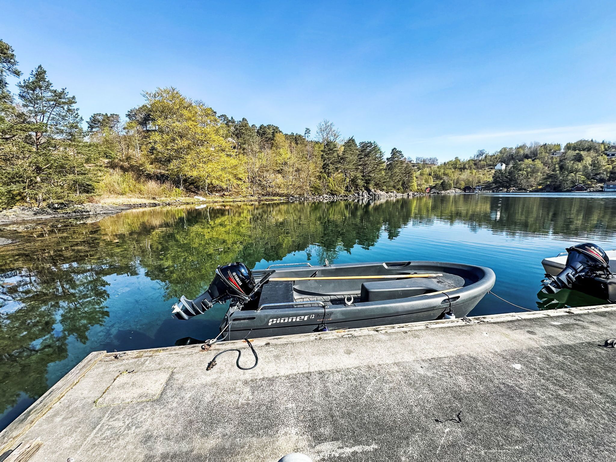A boat docked at a concrete pier with a calm lake and trees in the background.