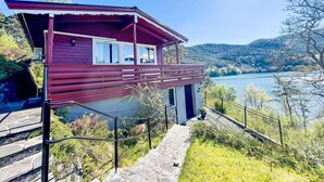 A red wooden cabin with a balcony overlooking a lake, surrounded by greenery and hills. - Tussebu by Interhome (Tysnes)
