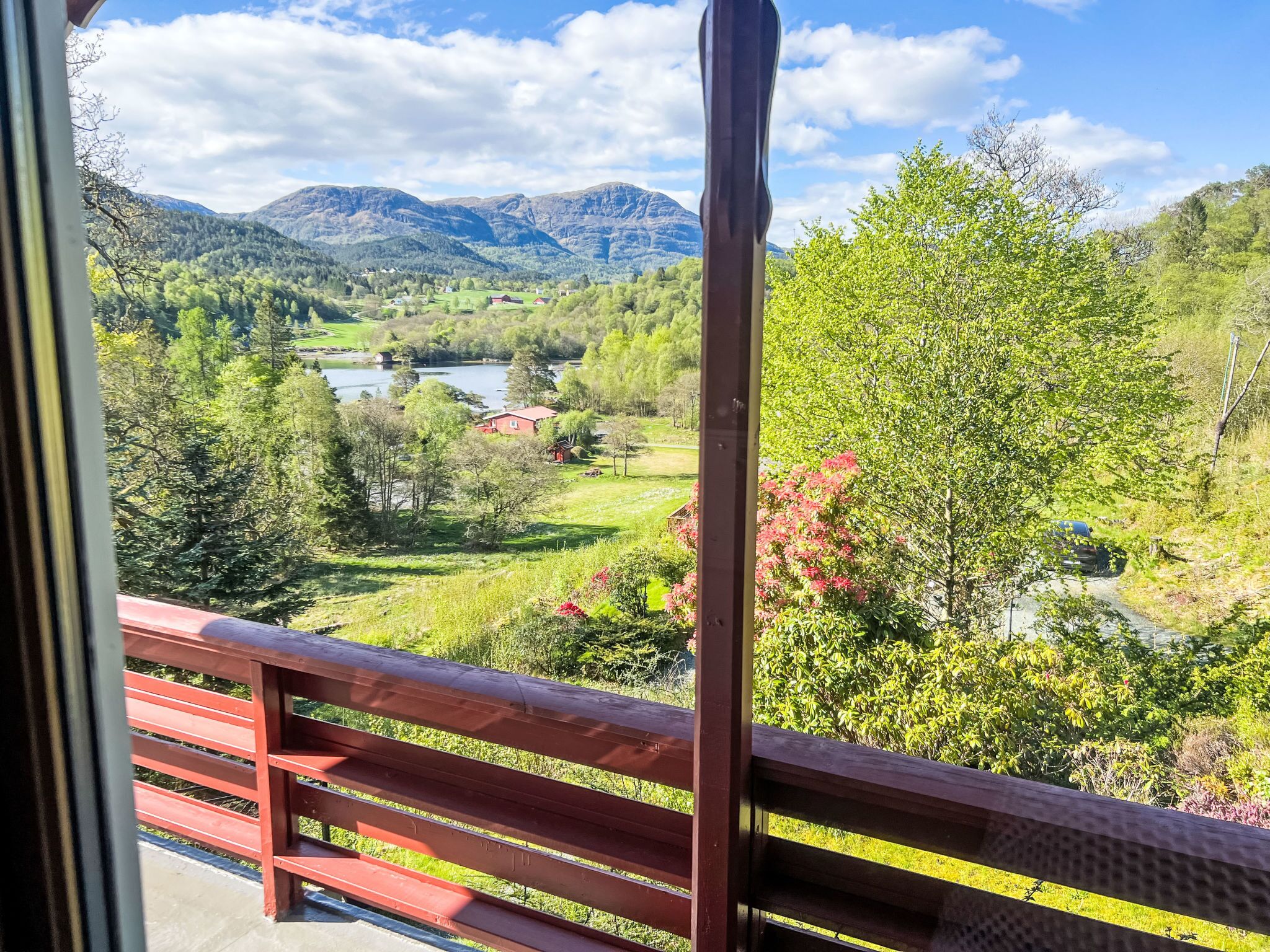 A balcony with a view of a mountainous landscape, a river, and a red building.