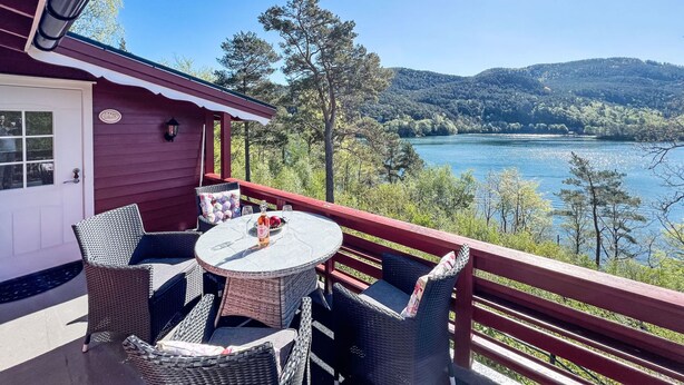 A covered deck with wicker furniture and a table, overlooking a lake and forested hills. - Tussebu by Interhome (Tysnes)