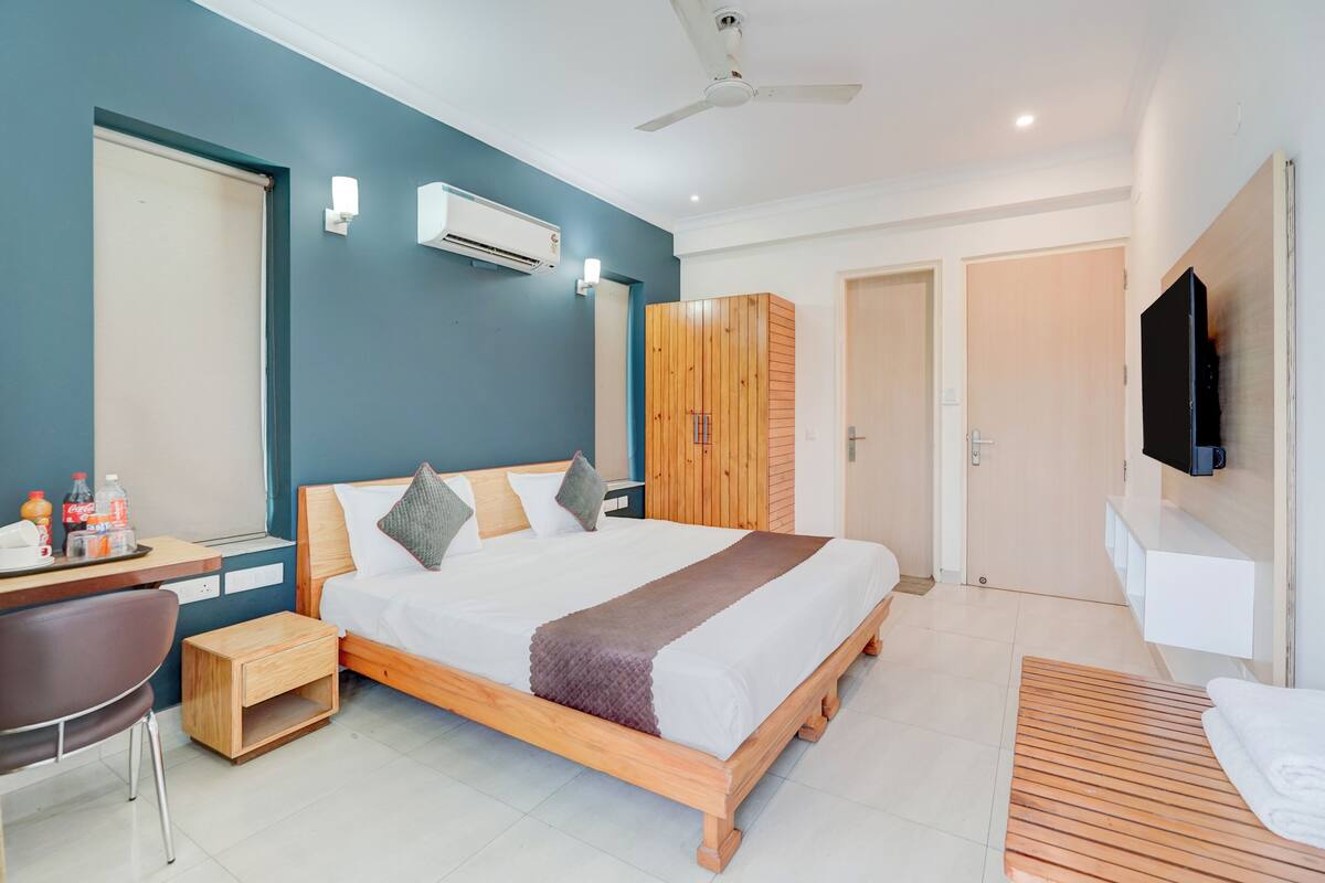 Una habitación de hotel moderna con una cama de madera, un escritorio con una silla, un televisor en la pared y un ventilador de techo.