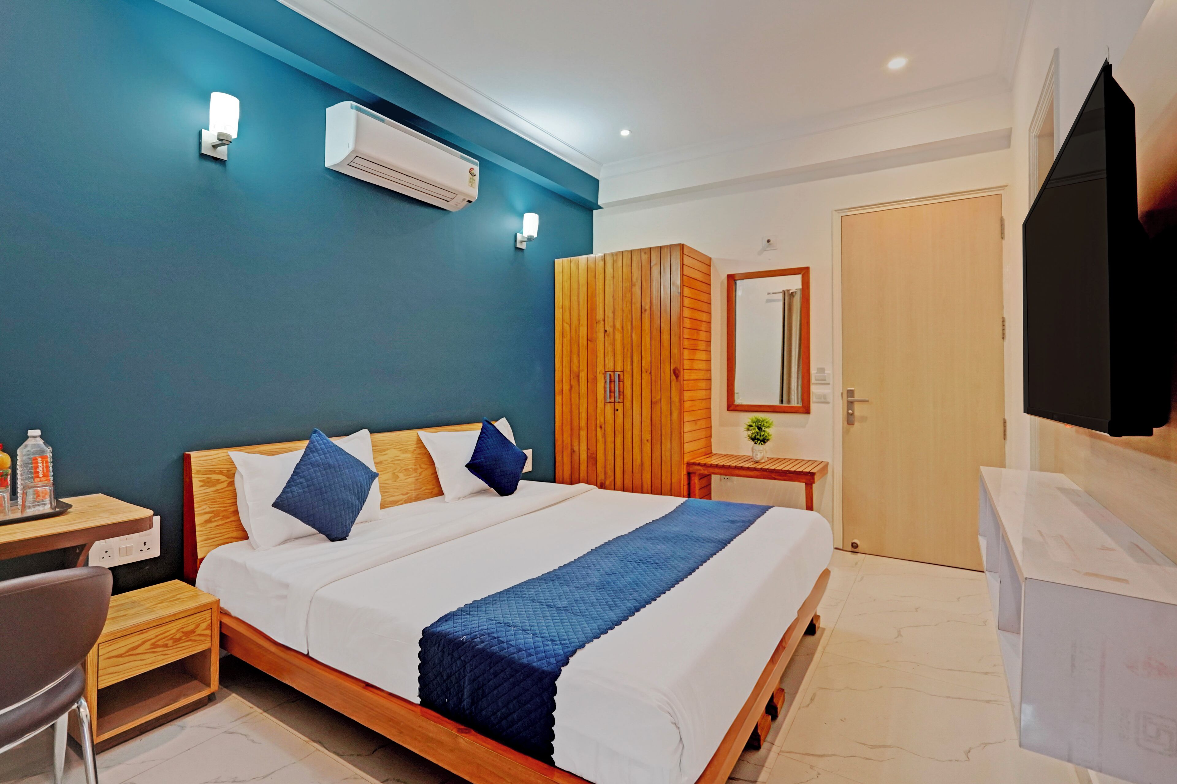 Una habitación de hotel moderna con una cama grande, un armario de madera y un televisor de pantalla plana montado en la pared.