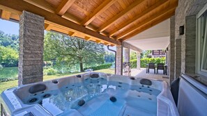Ein Whirlpool unter einer Holzw pergola mit Steinpfeilern, mit Blick auf einen angelegten Garten und einen See.