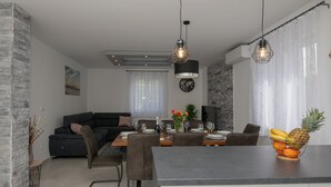 A modern living room with a dark sofa, a dining table set for four, and a kitchen area with a fruit bowl.