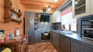Eine kompakte Küche mit Holzschränken, einem eingebauten Backofen, einem Geschirrspüler und einem Edelstahlkühlschrank.