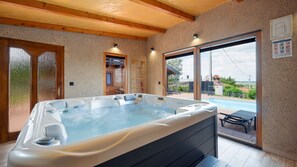 A hot tub in a room with wooden beams, a sliding glass door to a patio, and a view of a swimming pool. - Villa Luna - Ludbreg by Villas Guide (Ludbreg)